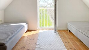 A bedroom with two beds, wooden flooring, a white carpet, and a large window with a view of trees. - 4 Star Holiday Home in Skivarp (Skivarp)