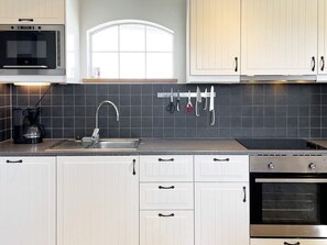 A modern kitchen with white cabinets, a black countertop, a window above the sink, and a coffee maker. - 4 Star Holiday Home in Skivarp (Skivarp)