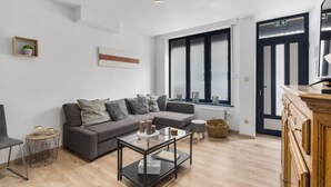 A modern living room with a grey sofa, a glass coffee table, and a wooden cabinet. - Beachfront Holiday Home Near the Market (Blankenberge)