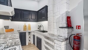 A compact kitchen with dark cabinets, a white backsplash, and a fire extinguisher mounted on the wall. - Beachfront Holiday Home Near the Market (Blankenberge)