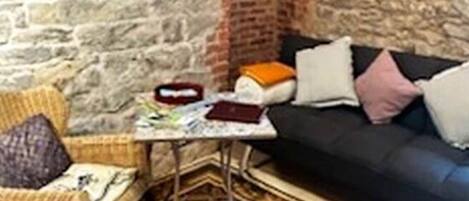 A cozy room with a stone wall, a black sofa, a wicker chair, and a patterned rug.