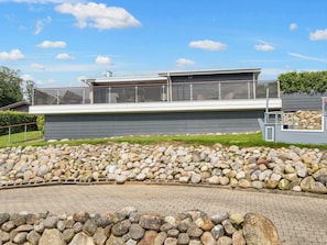 A modern building with a flat roof, a balcony, and a stone retaining wall. - 8 Person Holiday Home in Aabenraa (Aabenraa)
