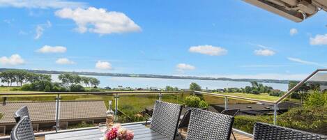 An outdoor patio with a table and chairs, overlooking a body of water and a distant landscape.