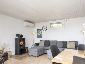 A modern living room with a sectional sofa, a fireplace, a clock, and a framed picture on the wall. - 8 Person Holiday Home in Aabenraa (Aabenraa)