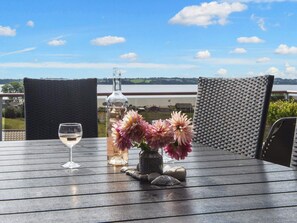 A wooden table with a glass bottle, a glass of white wine, and pink flowers.