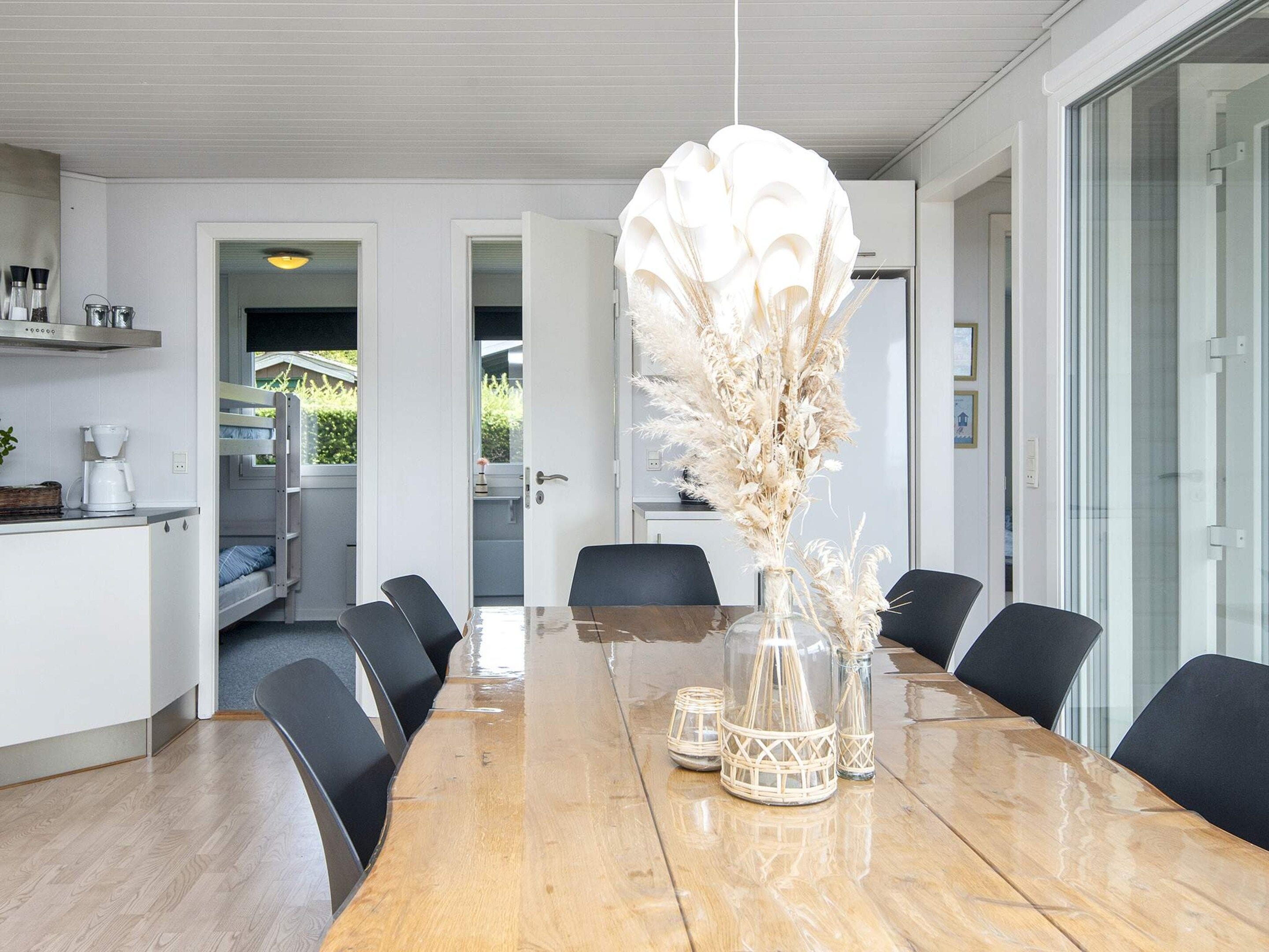 A modern dining area with a wooden table, black chairs, and a decorative vase with dried plants.