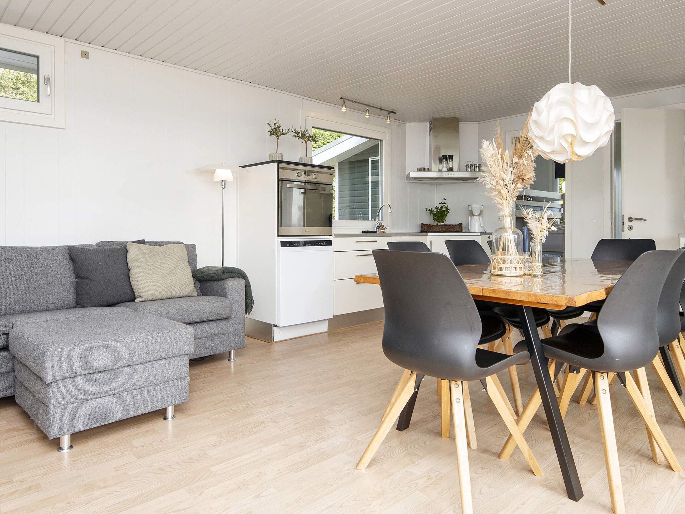 A modern living space with a grey sofa, wooden dining table, and black chairs.