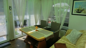 A cozy living room with a sofa, a dining table with chairs, and a window with curtains. - "min Hus" Quiet and Close to the Beach (Zingst)