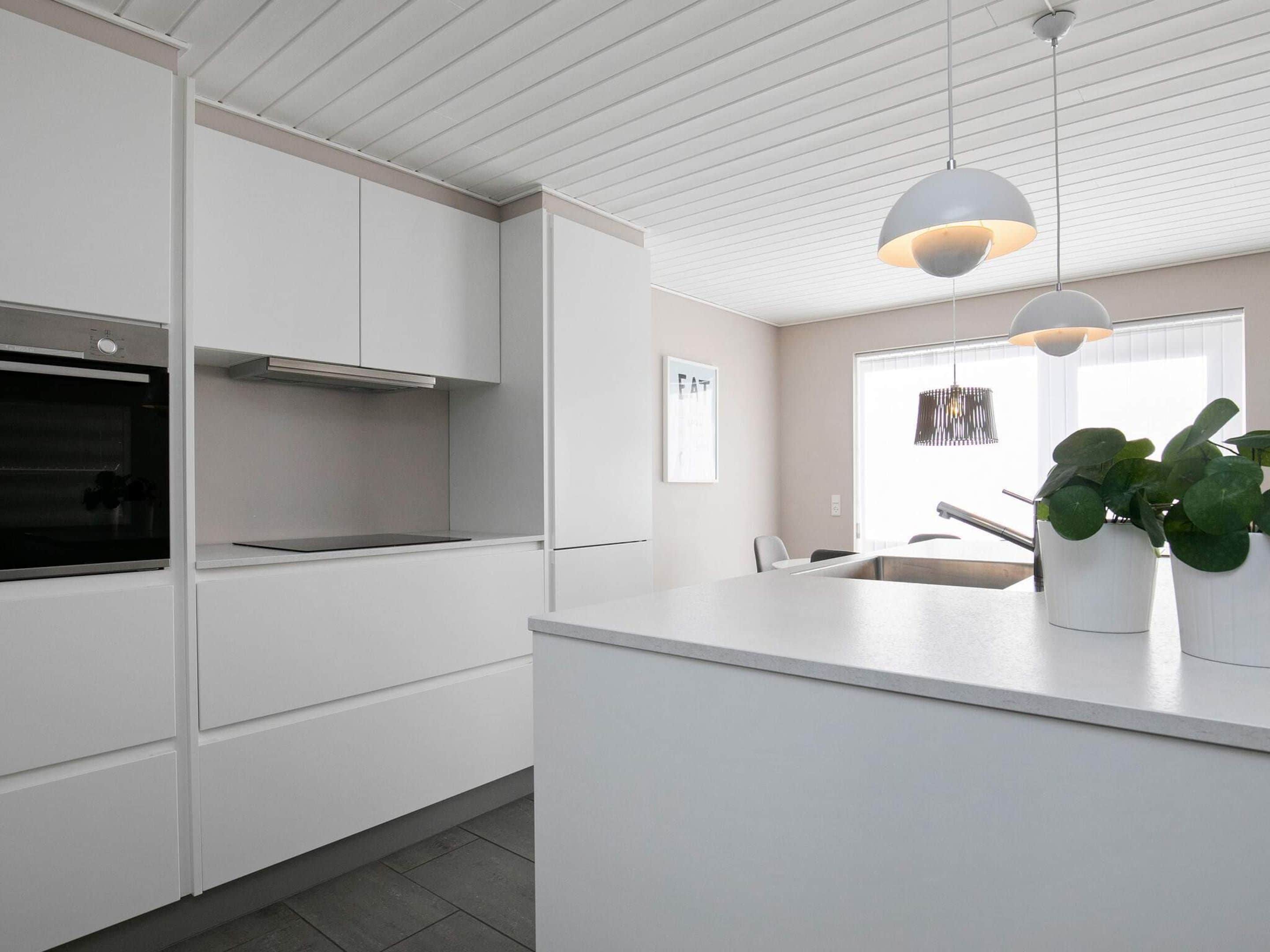 A modern kitchen with white cabinetry, a built-in oven, pendant lighting, and a large window.