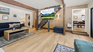 A modern living room with a wooden staircase, a flat-screen TV mounted on a wall, a sofa, a coffee table, and a rug.