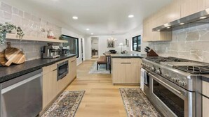 A modern kitchen with a central island, stainless steel appliances, and light wood cabinetry.