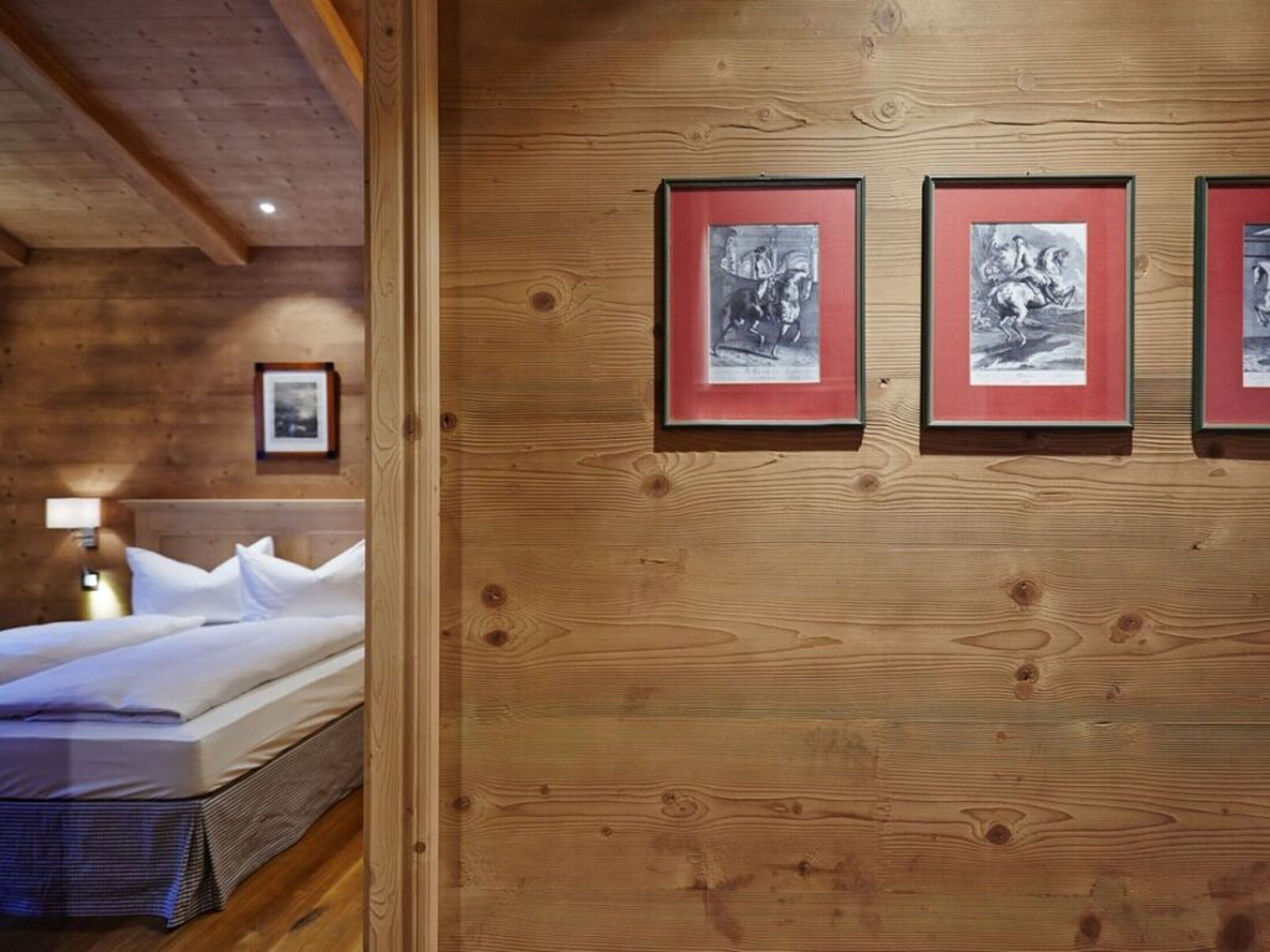 A wooden-paneled room with a bed, a nightstand, and three framed pictures on the wall.