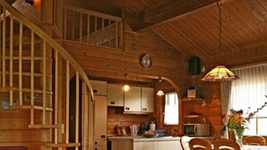 A cozy cabin interior with a wooden staircase, a dining area with a table and chairs, a kitchen with cabinets and a sink, and a living room with a sofa and a plaid tablecloth. - Holiday Home Anja in Motten (Motten)