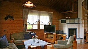 A cozy cabin-style room with a wooden interior, a sofa, a chair, a small table, and a television. - Holiday Home Anja in Motten (Motten)