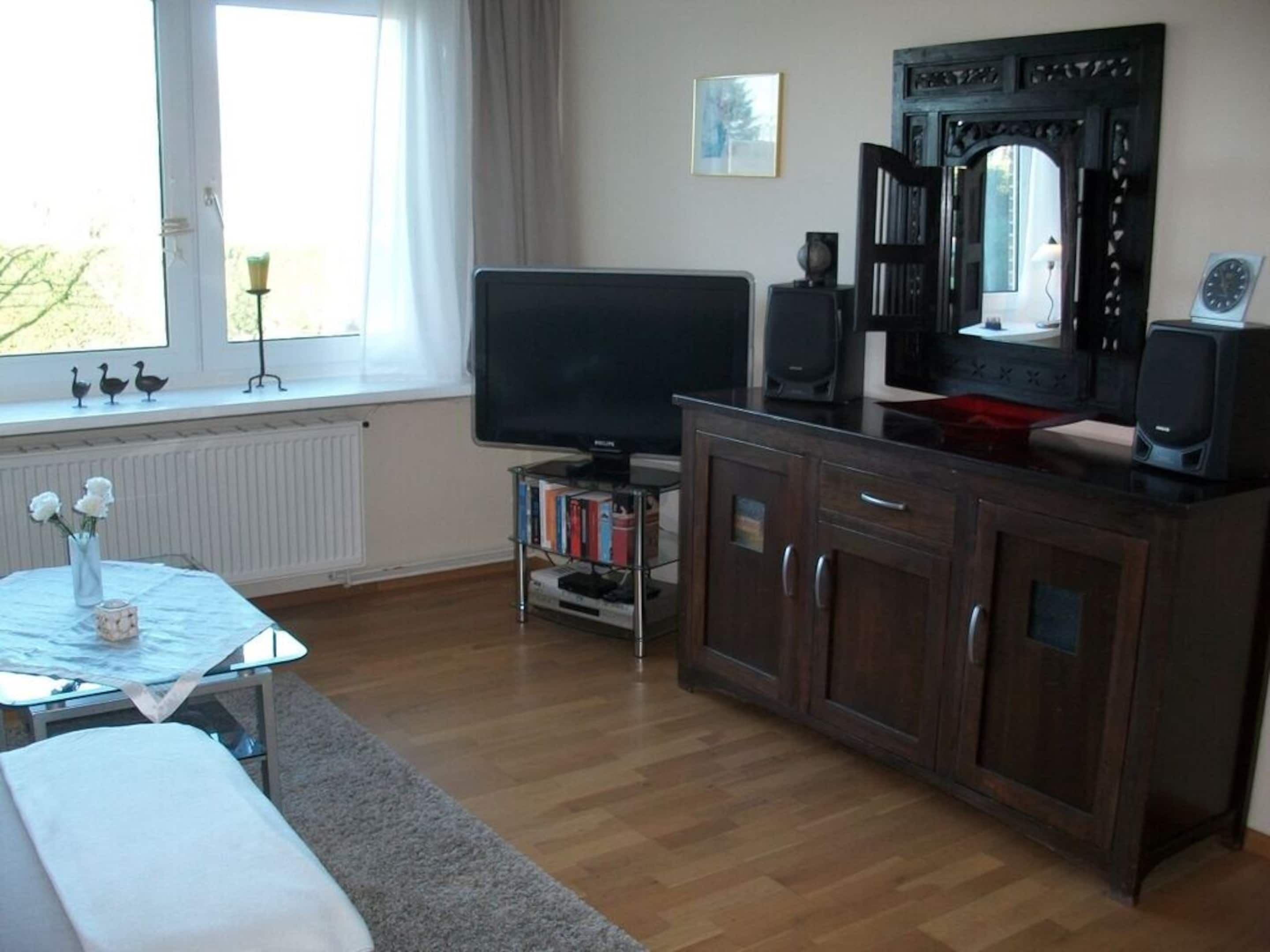 A living room with a flat-screen TV, wooden cabinet, and a bookshelf.