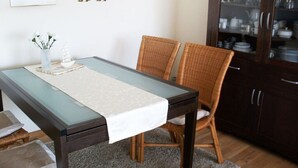 Un coin repas comprenant une table à plateau en verre, des chaises en osier, un chemin de table blanc et un buffet aux portes en verre.