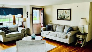 A living room with two sofas, a coffee table, and a side table with books. - Last minute Cape cod rental
  Bikes,  Beach ,ac  ,laundry ,ping pong table  (Dennis)