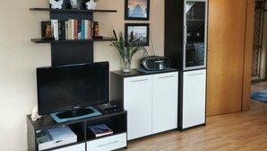 A living room with a flat-screen TV, a cabinet with a radio, and a bookshelf with books and decorative items. - "haus Burck" Modern Retreat (Wankendorf)