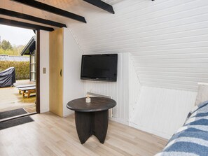 A room with a television mounted on the wall, a round table, and a view of the outdoors through a door.