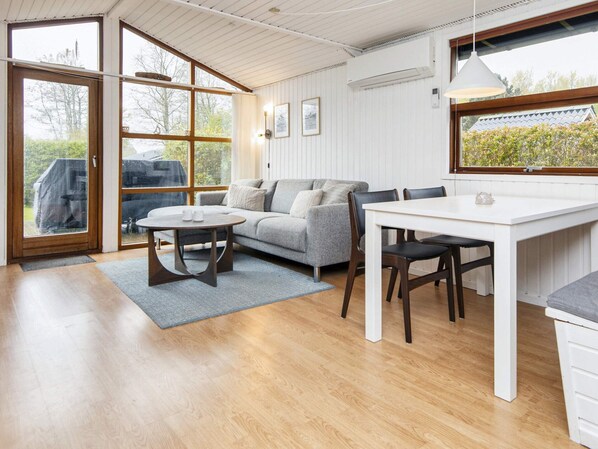 A modern interior with a sofa, dining table, and chairs, large windows, and an air conditioning unit.