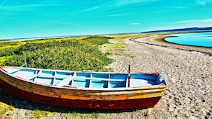 En båd ved en stenet strand med en sø og skov i baggrunden.