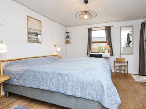 A bedroom with a large bed, a desk, a chair, a lamp, a window with curtains, and a hanging light fixture. - 6 Person Holiday Home in Hemmet (Hemmet)