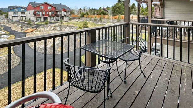 Une terrasse en bois avec une table et des chaises, donnant sur un quartier résidentiel avec des maisons et un ciel dégagé.