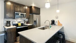 Une cuisine moderne avec des meubles de couleur bois foncé, des appareils en acier inoxydable, un grand îlot central doté de tabourets et un éclairage suspendu.