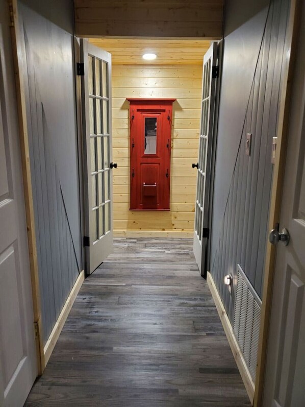 A hallway with wooden walls, a red door, and a grey floor. - Iconic A-Frame in Spruce Sands (Gimli)