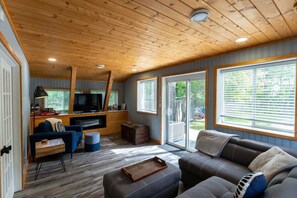Una sala de estar acogedora con techo de madera, televisor, sofá y un amplio ventanal.