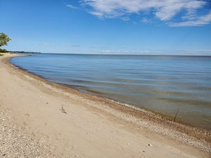 A beach with clear water, a sandy shore, and a distant shoreline. - Iconic A-Frame in Spruce Sands (Gimli)