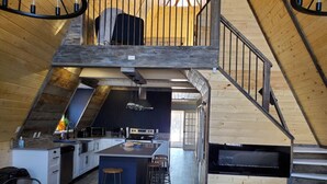 Une cuisine de style industriel, avec un îlot central, des poutres en bois et un escalier menant à un niveau supérieur.