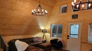 L’intérieur d’un chalet accueillant, avec un plafond en bois, un grand canapé, une petite table et une pancarte sur laquelle on peut lire : « Happy Place Lake ».