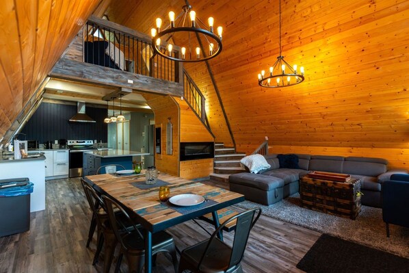 A cozy cabin interior with a dining area, kitchen, and a staircase leading to an upper level. - Iconic A-Frame in Spruce Sands (Gimli)
