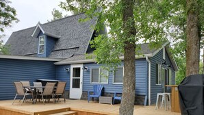 Une maison bleue avec une terrasse en bois, du mobilier d’extérieur et un barbecue.
