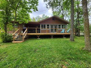 Une cabane en bois à deux étages, dotée d’une terrasse et entourée d’arbres.