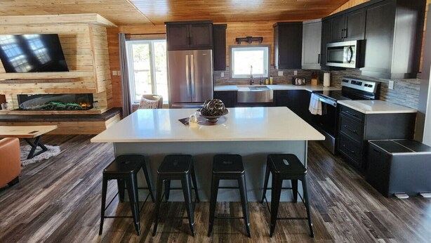 Een moderne keuken met een centraal eiland, zwarte barkrukken, roestvrijstalen apparatuur en een houten plafond.