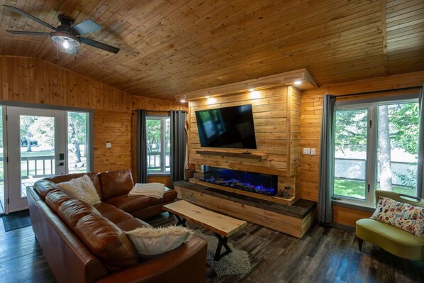 A wooden interior with a leather sofa, a flat-screen TV mounted on a wooden wall, and a fireplace. - Ultimate vacation lodge (Gimli)