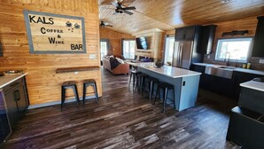 Een moderne keuken met houten vloeren, een centraal eiland met krukken, een bar en een bordje voor Kals Coffee & Wine Bar.