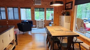 A spacious wooden cabin interior with a dining area, kitchen, and large windows. - The Birch Grove Escape (Gimli)