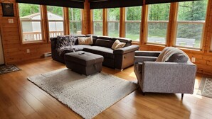A cozy living room with a sectional sofa, a loveseat, and a chair. There are large windows providing a view of the outdoors. - The Birch Grove Escape (Gimli)