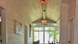 A hallway with wooden walls and a ceiling fan, leading to a dining area with a table and chairs. - Boho Luxe Lakefront Cottage (Gimli)