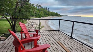 A wooden deck with red Adirondack chairs overlooking a body of water. - Boho Luxe Lakefront Cottage (Gimli)