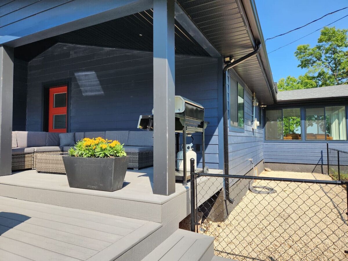Un espace extérieur abrité doté d’une terrasse grise, d’une porte rouge et d’un grand bac à fleurs contenant des fleurs jaunes.