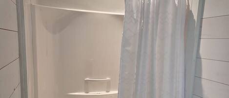 Un baño con ducha, inodoro y una alfombra blanca.