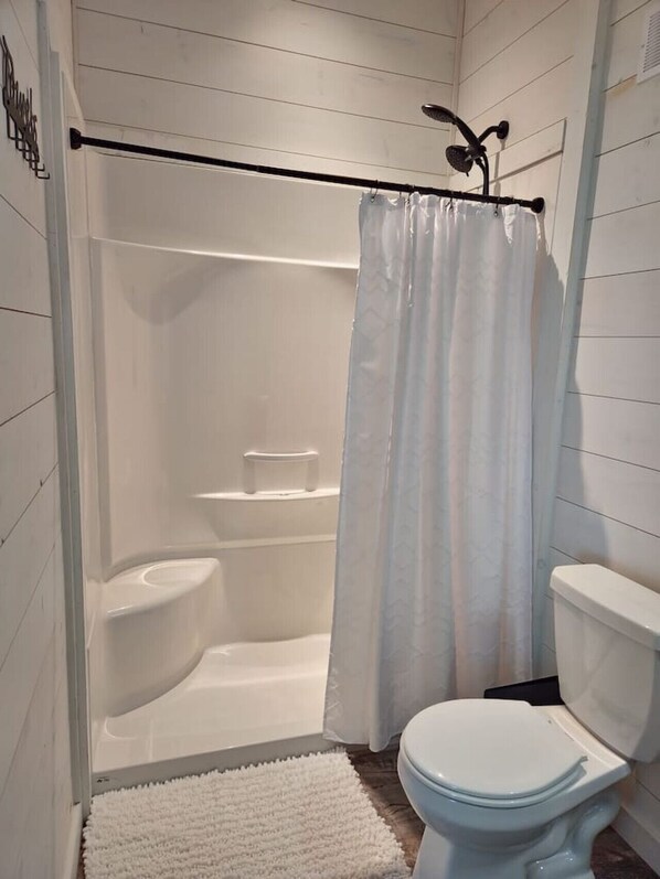 A bathroom with a shower, toilet, and a white rug. - Boho Luxe Lakefront Cottage (Gimli)