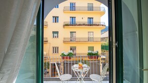 Un balcón con mesa y sillas, un edificio amarillo con balcones y una ventana con cortina.