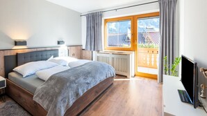 A modern bedroom with a large bed, wooden headboard, and a view of a balcony with curtains. - Great Apartment Near the ski Area (Schwendau)
