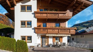 A multi-story chalet with wooden balconies, a covered terrace, and a mountainous backdrop. - Great Apartment Near the ski Area (Schwendau)