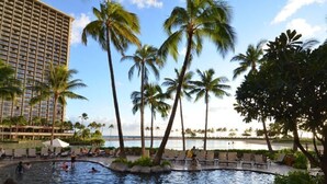 Ein Hotelpoolbereich mit Palmen, Liegestühlen und Blick aufs Meer.